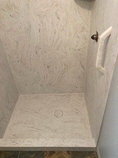 A shower stall with a marble wall and floor in a bathroom.