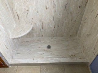 A shower stall with a seat and a drain in a bathroom.