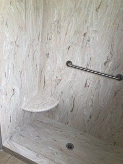 A walk in shower with a seat and a hand rail.