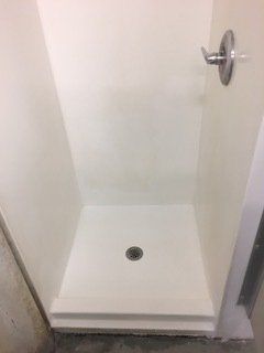 A white shower stall with a drain and a shower head.