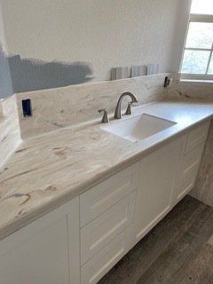 A kitchen with a sink , cabinets , counter tops and a window.