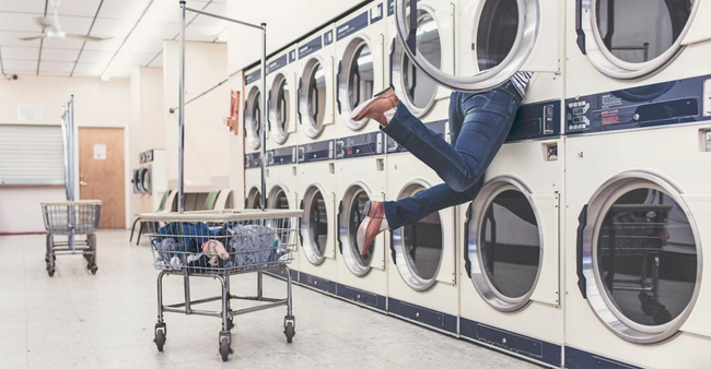 A person is jumping out of a washing machine in a laundromat.