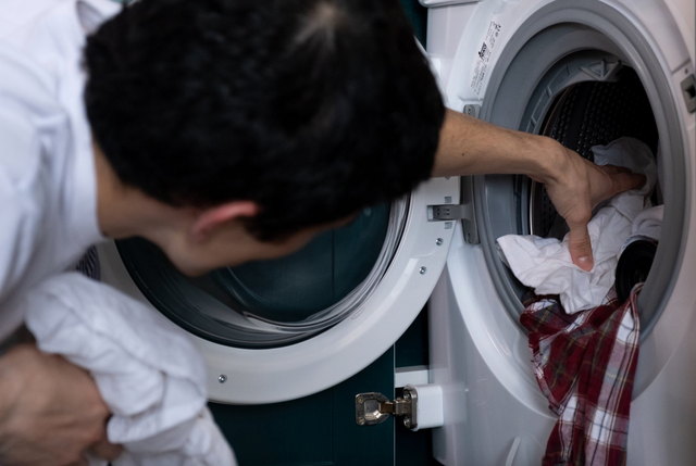 A man is putting clothes in a washing machine.