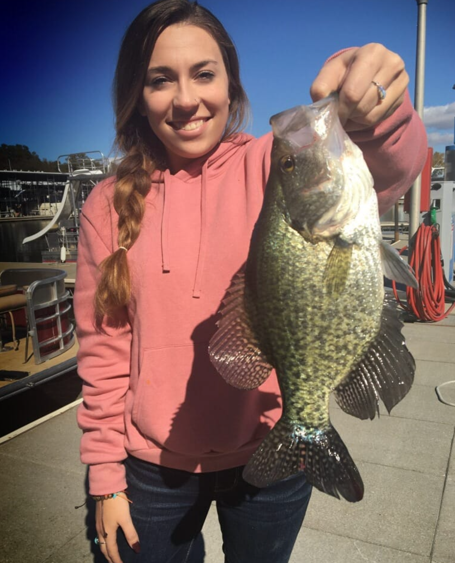 A woman in a pink hoodie is holding a large fish