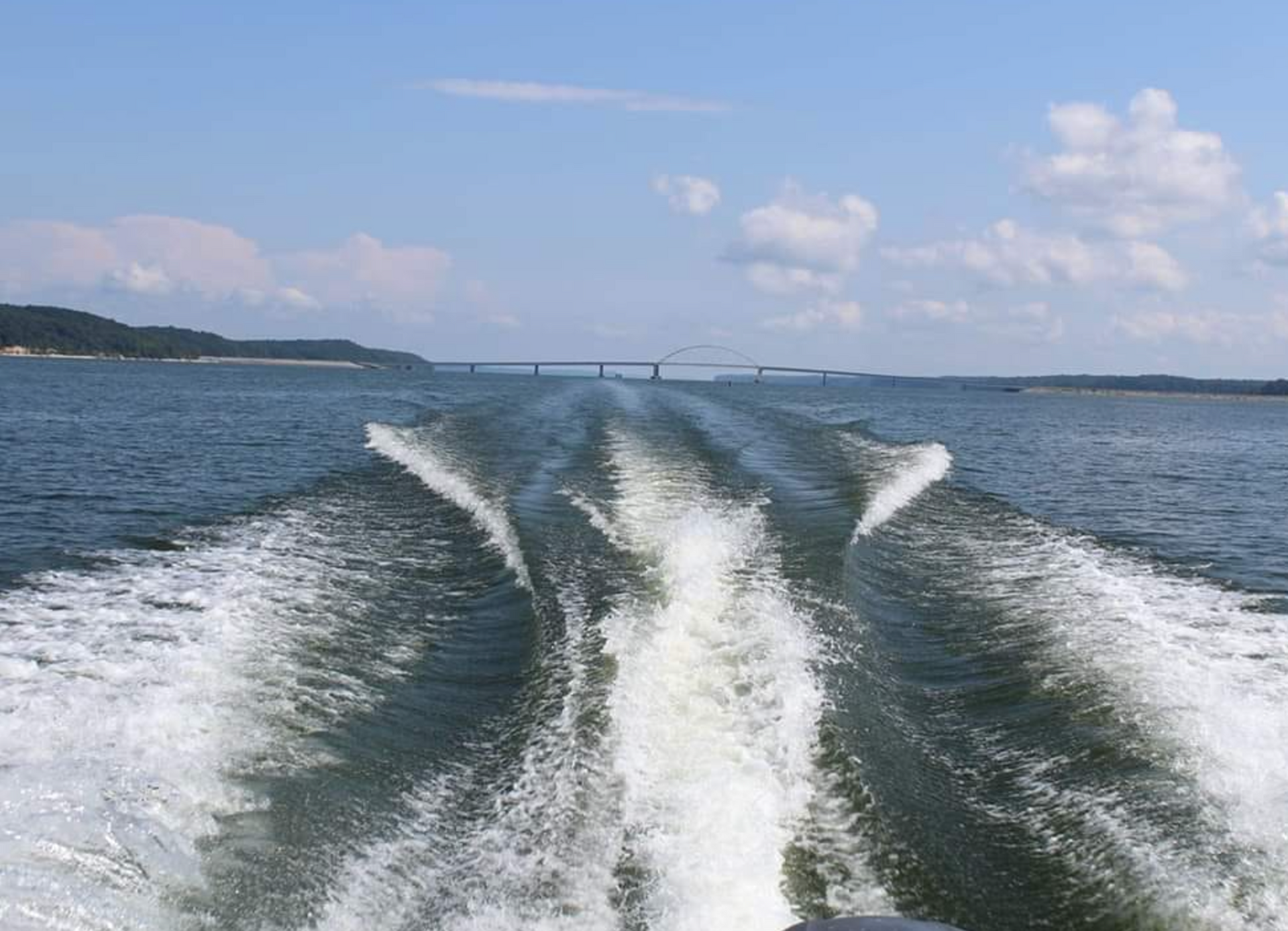A boat is going through the water with a bridge in the background