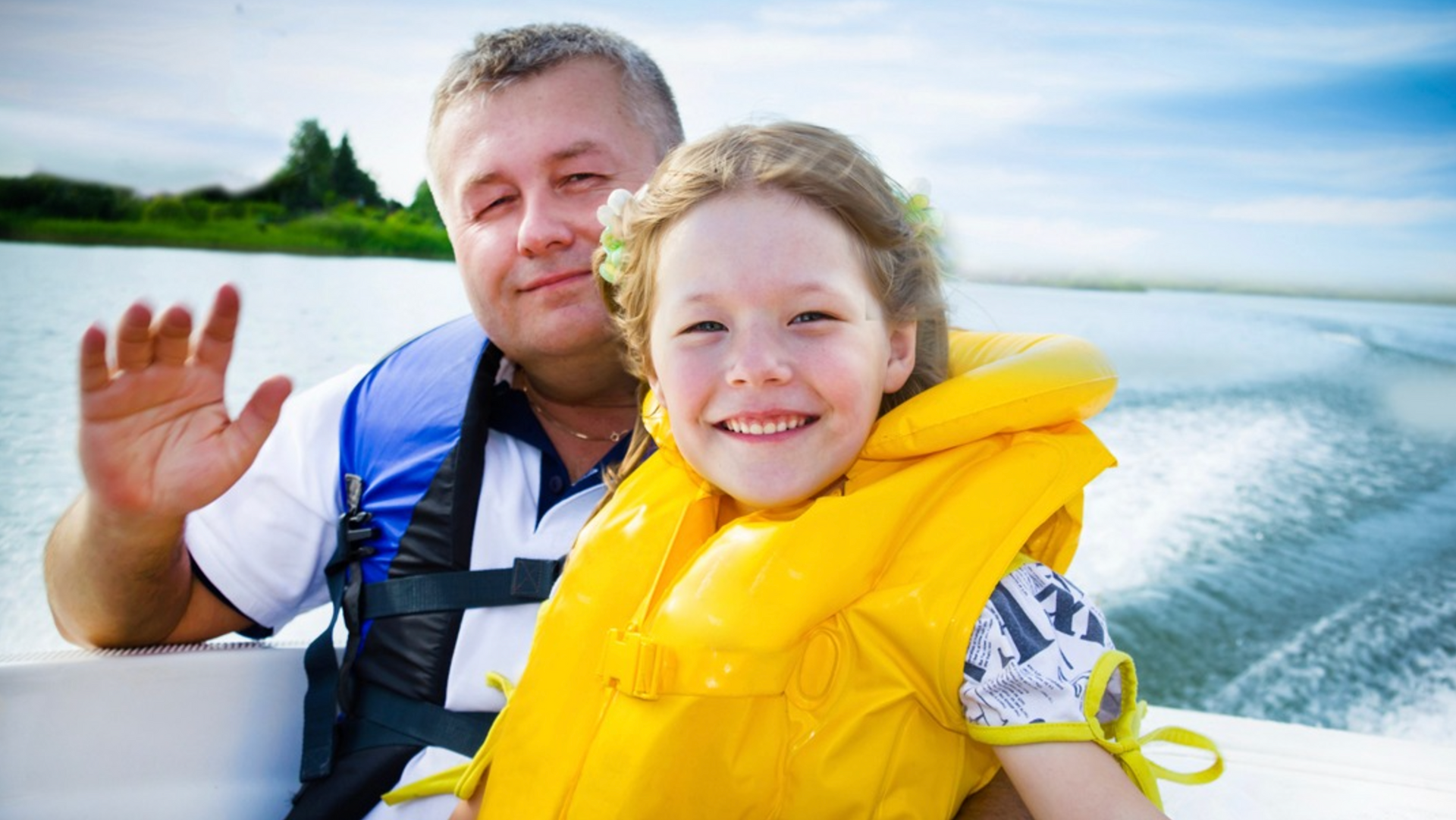 A man and a little girl are sitting on a boat wearing life jackets.