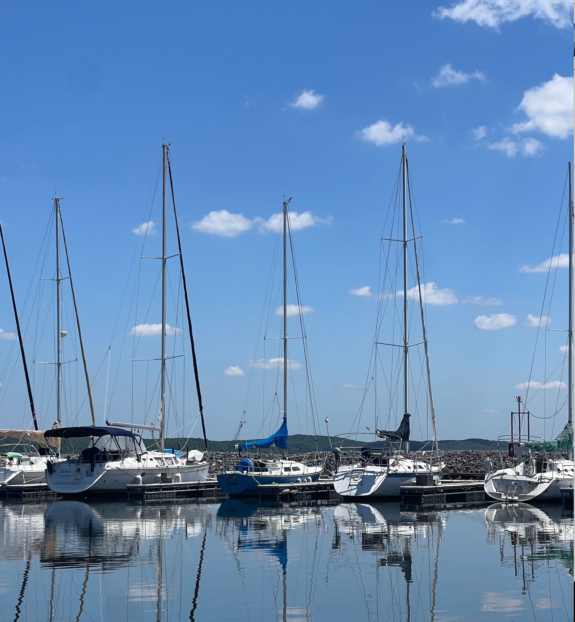 A row of sailboats are docked in a harbor on a sunny day