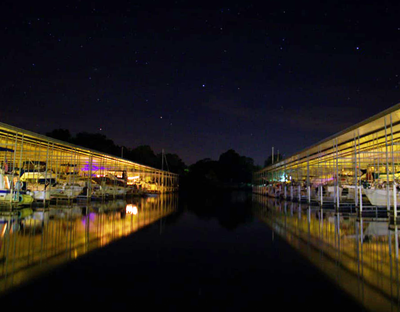 A row of boats are docked at a marina at night.
