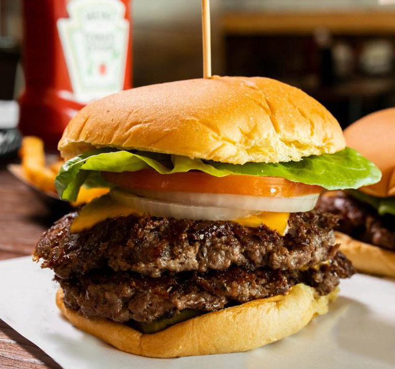 A double cheeseburger with lettuce tomato and onions on a bun