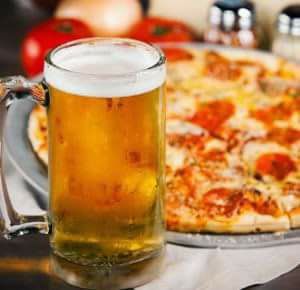 A glass of beer is sitting next to a pizza on a table.