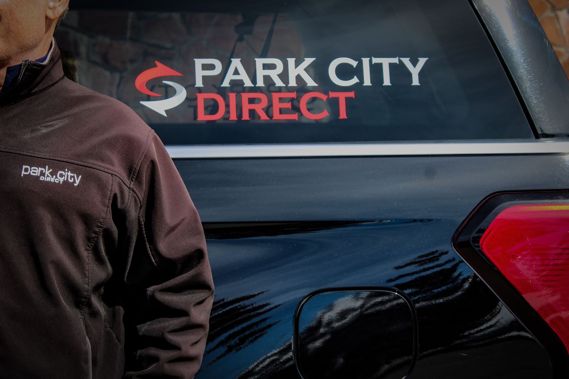A man is standing in front of a park city direct vehicle.