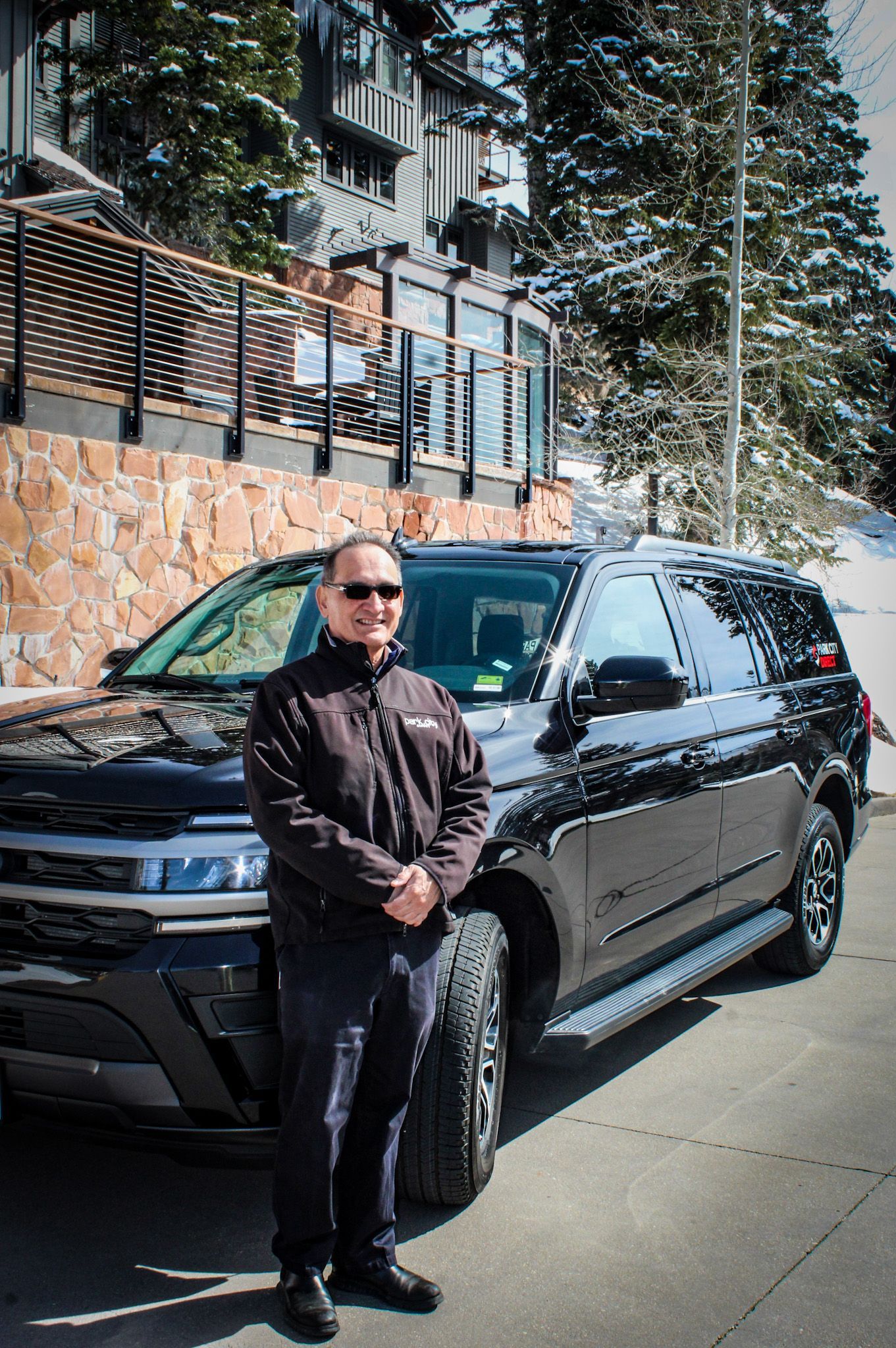 A man wearing sunglasses is standing next to a black suv