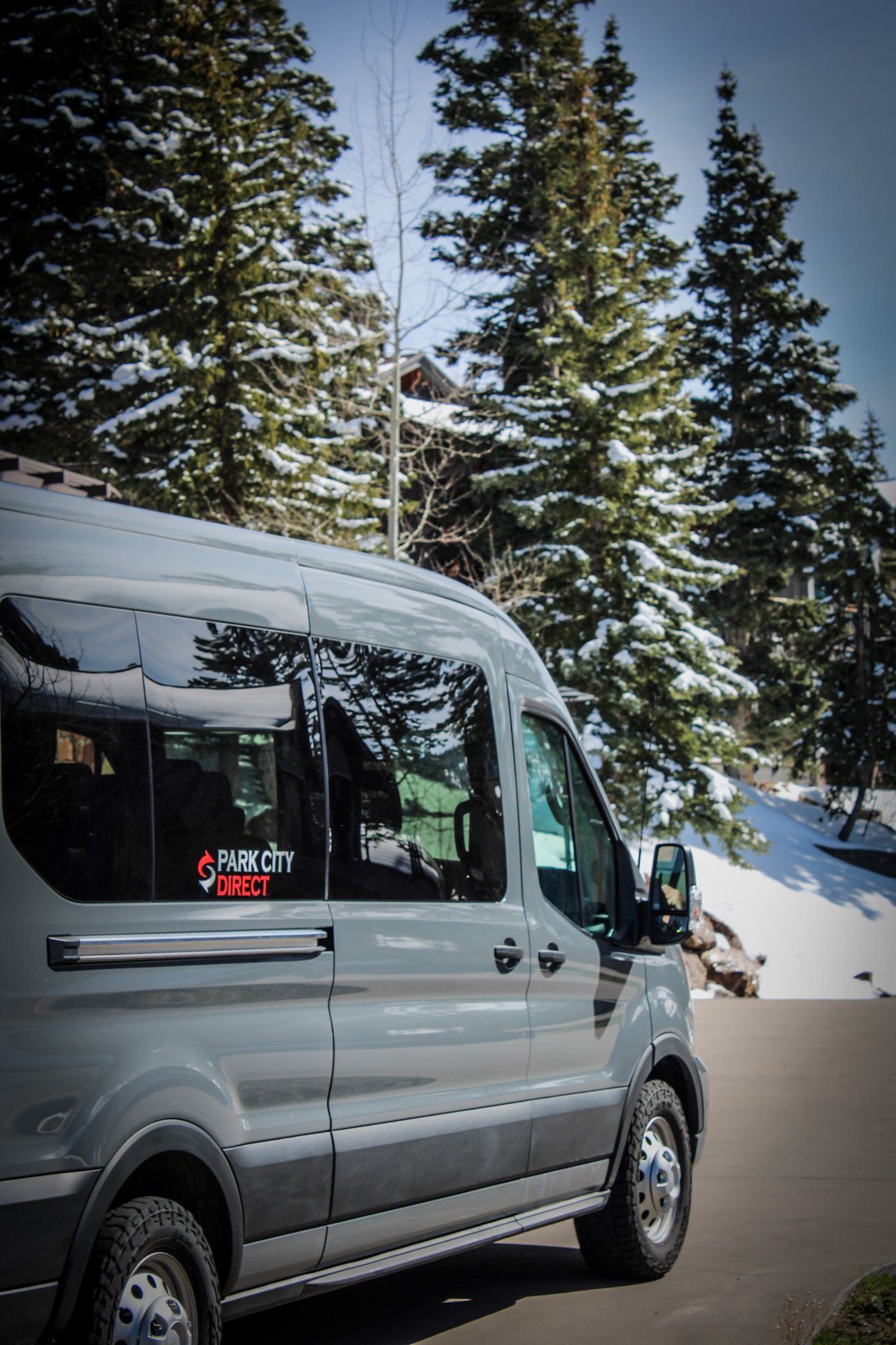 A van is parked on the side of the road in front of snow covered trees.