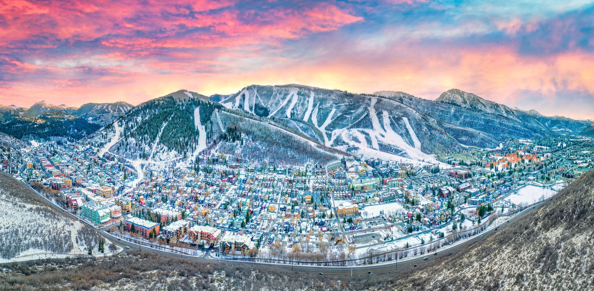 Snow-covered mountain range with Park City Ski Resort under a colorful sunset sky.