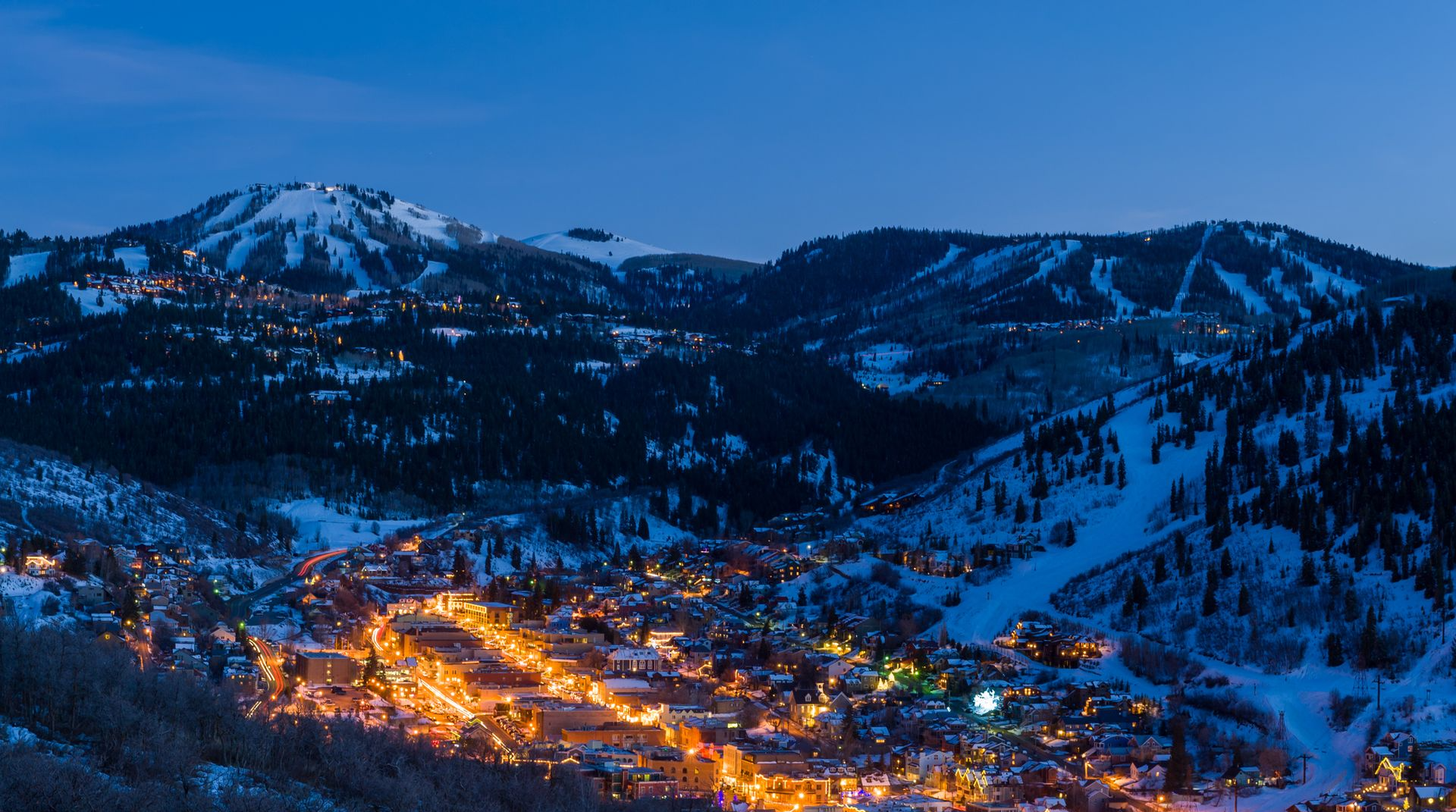 Snowy mountain town lit with orange lights at dusk.