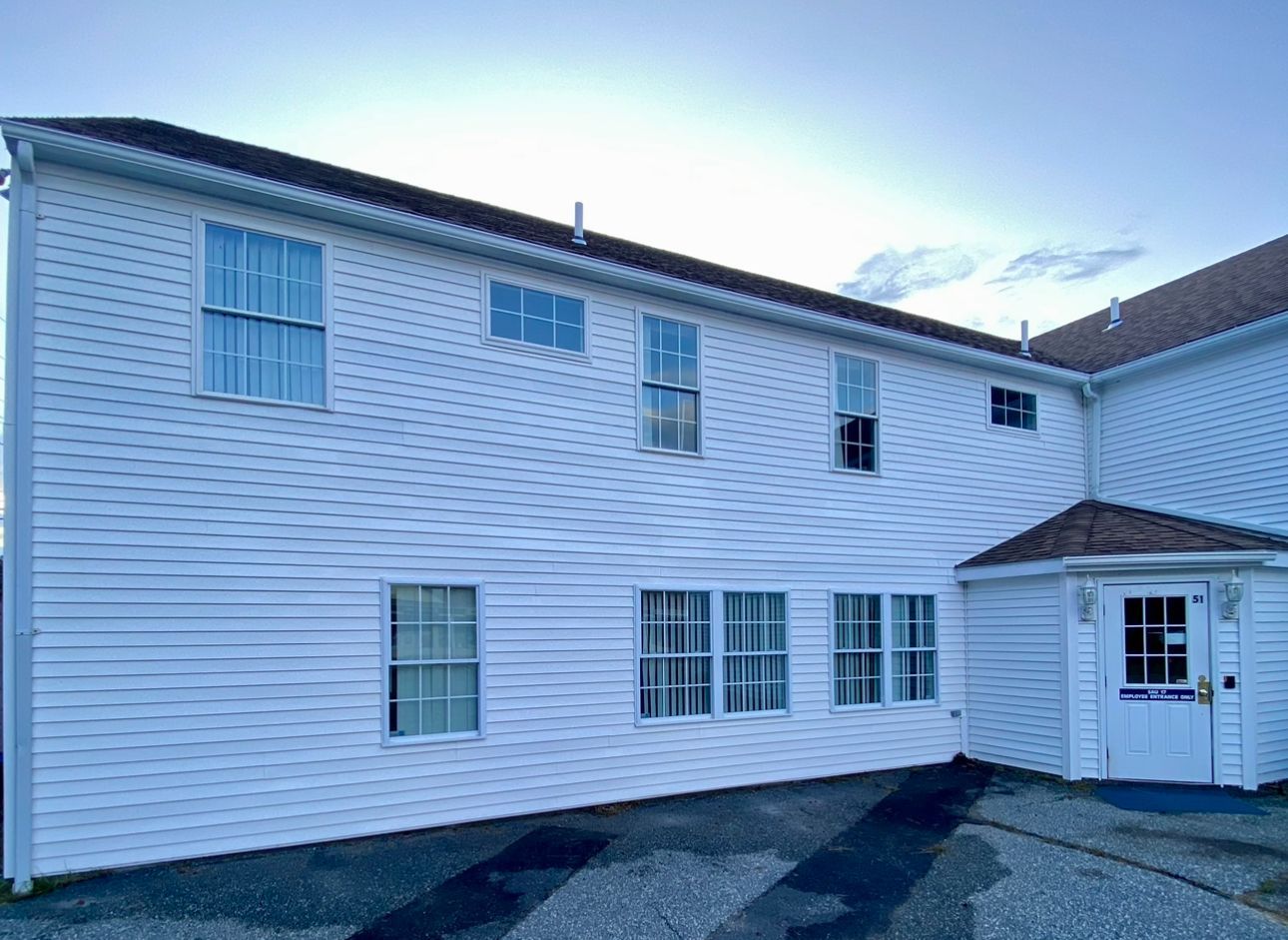 Three workers wearing safety harnesses and helmets clean the glass windows of a high-rise building while suspended by ropes.