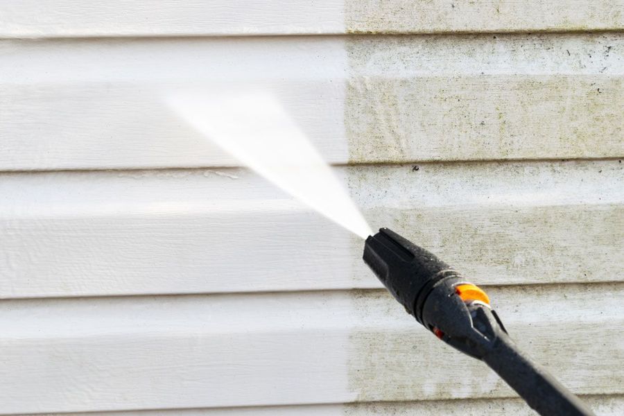 A person is cleaning a house with a high pressure washer.