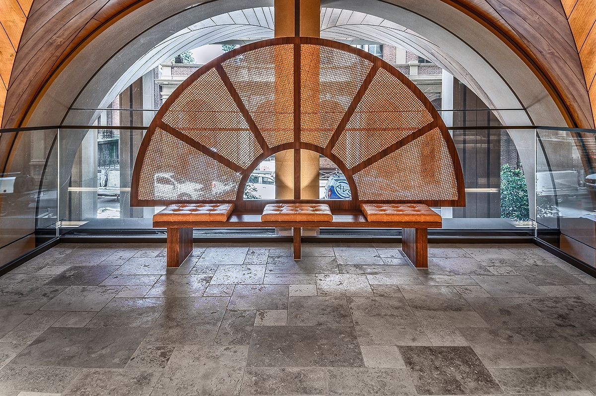Wooden bench beneath a semi-circular, patterned screen, within an arched window frame. Gray stone floor.