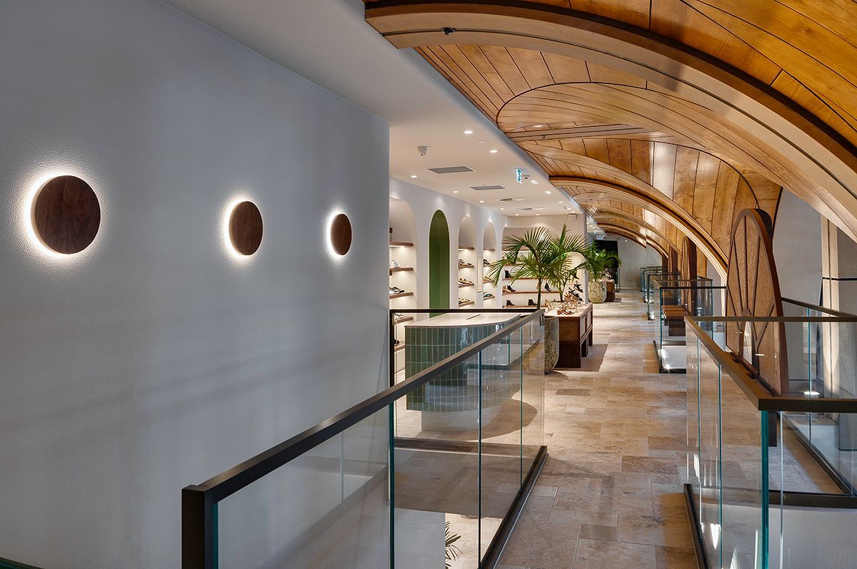 Hallway with glass railing, circular wall lights, arched wood ceiling, and store in the background.