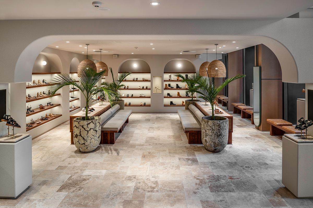 Shoe store interior with arched displays, benches, plants, and beige flooring.