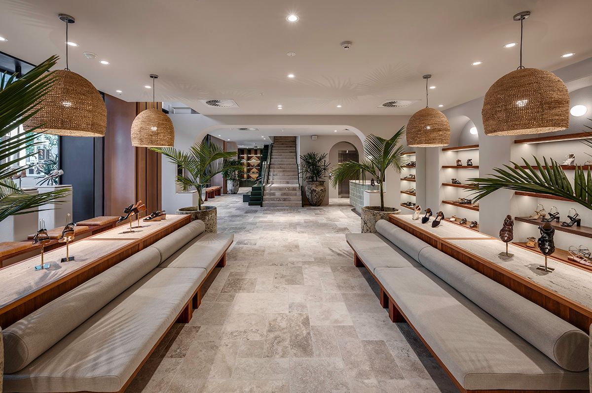 Interior of a store with display tables, benches, plants, and woven pendant lights.