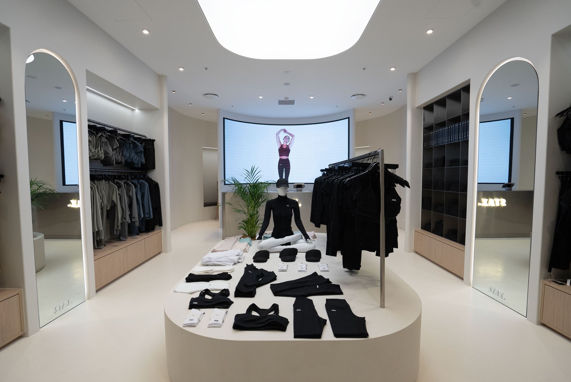 Clothing store interior with clothing displays and large screen showing person.