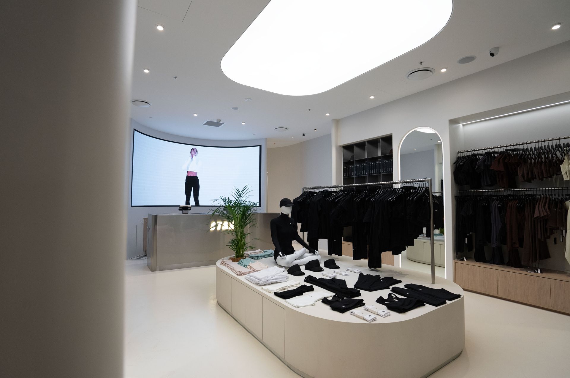 Clothing store interior with clothing displays, large screen showing a person, and modern white design.