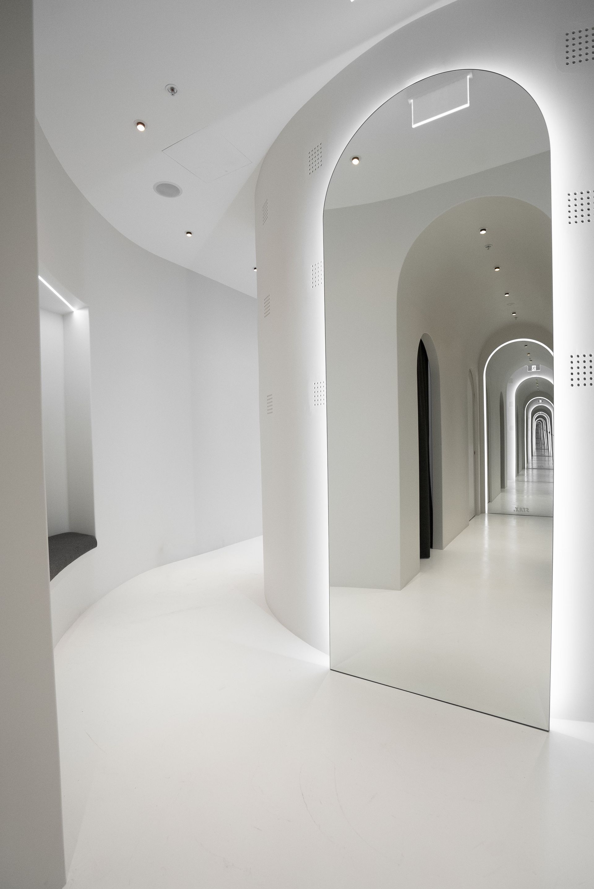 A long, curved white hallway with arched doorways and recessed lighting.