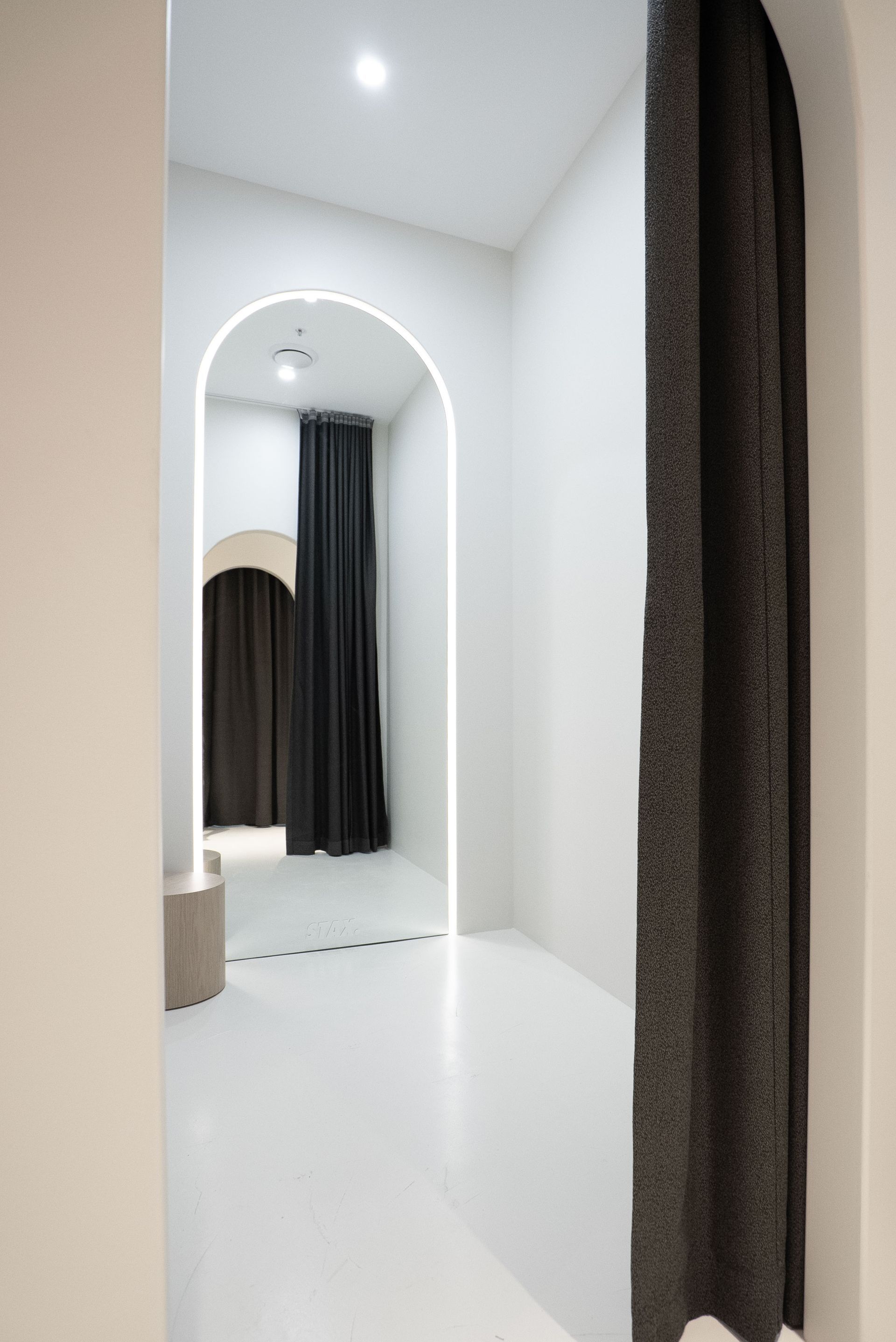 White room with archways, dark curtains, and a bright floor.