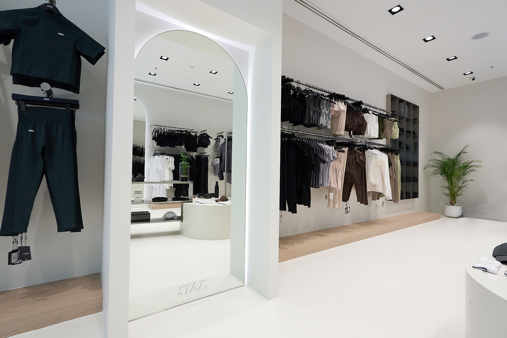 Clothing store interior with clothing racks, a large mirror, and white floors and walls.