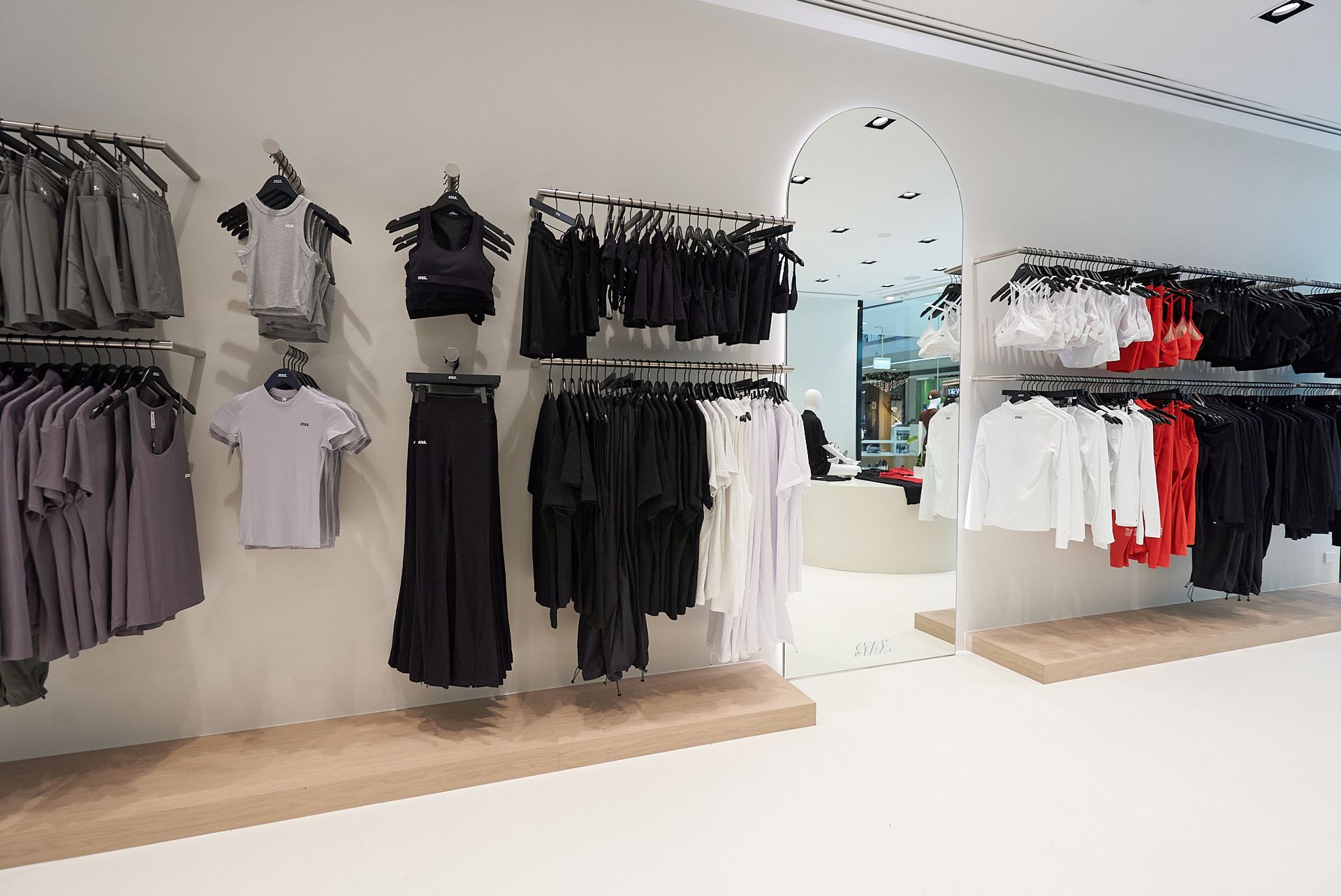 Clothing store interior with racks of black, white, and gray garments, a large arched mirror, and tan shelves.