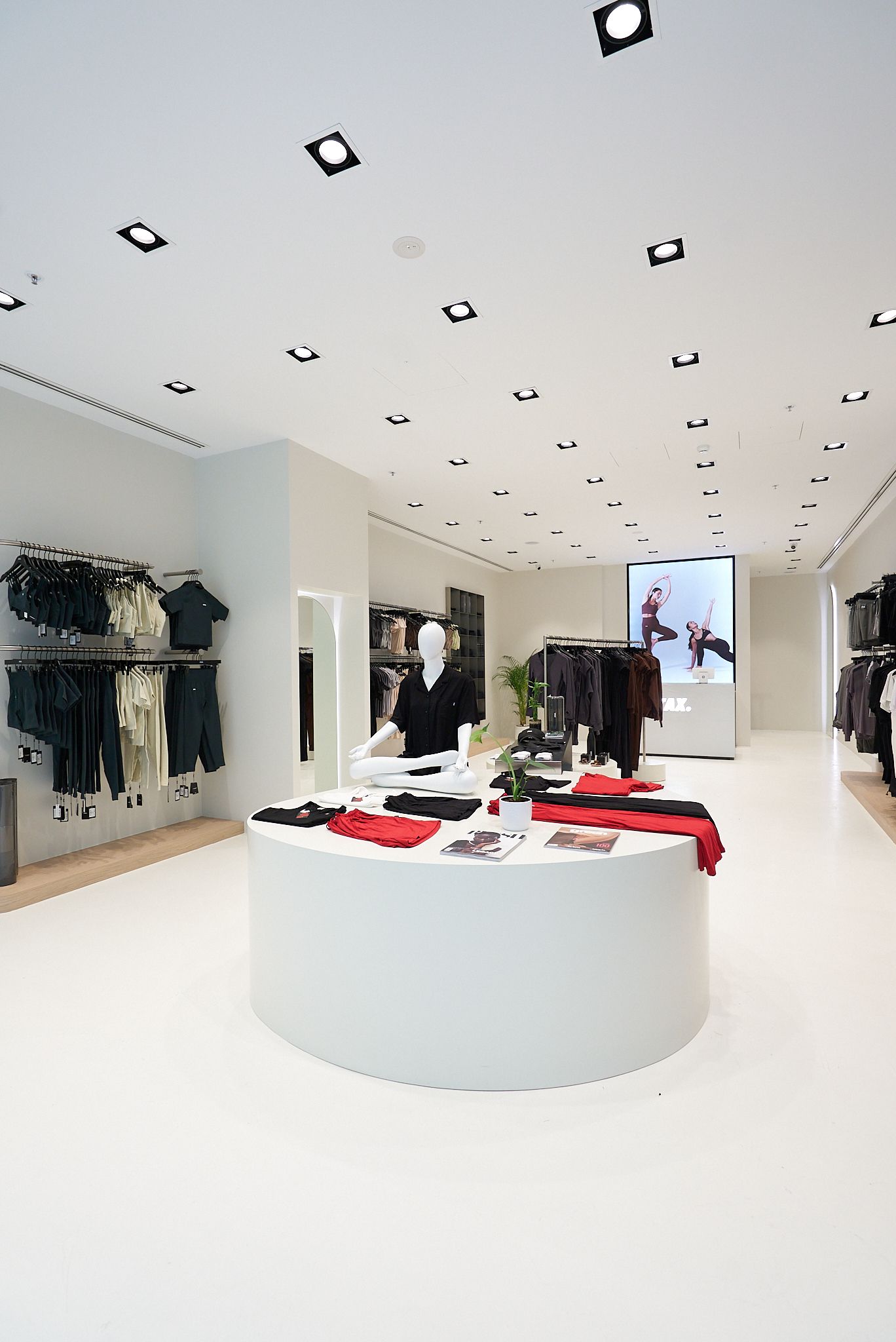 White clothing store interior with minimalist design; clothing displayed on racks and a circular display table.