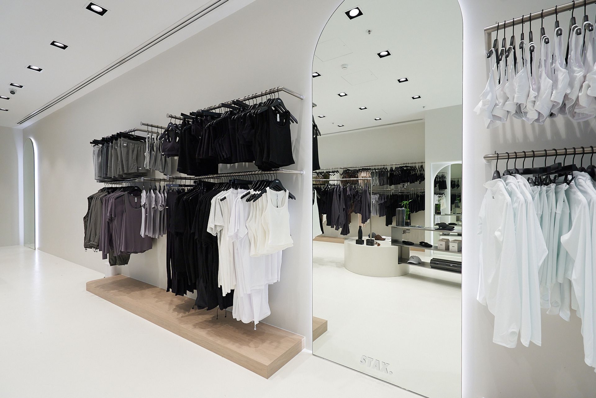Clothing store interior with racks of black and white clothing, large mirror, and bright white floor.
