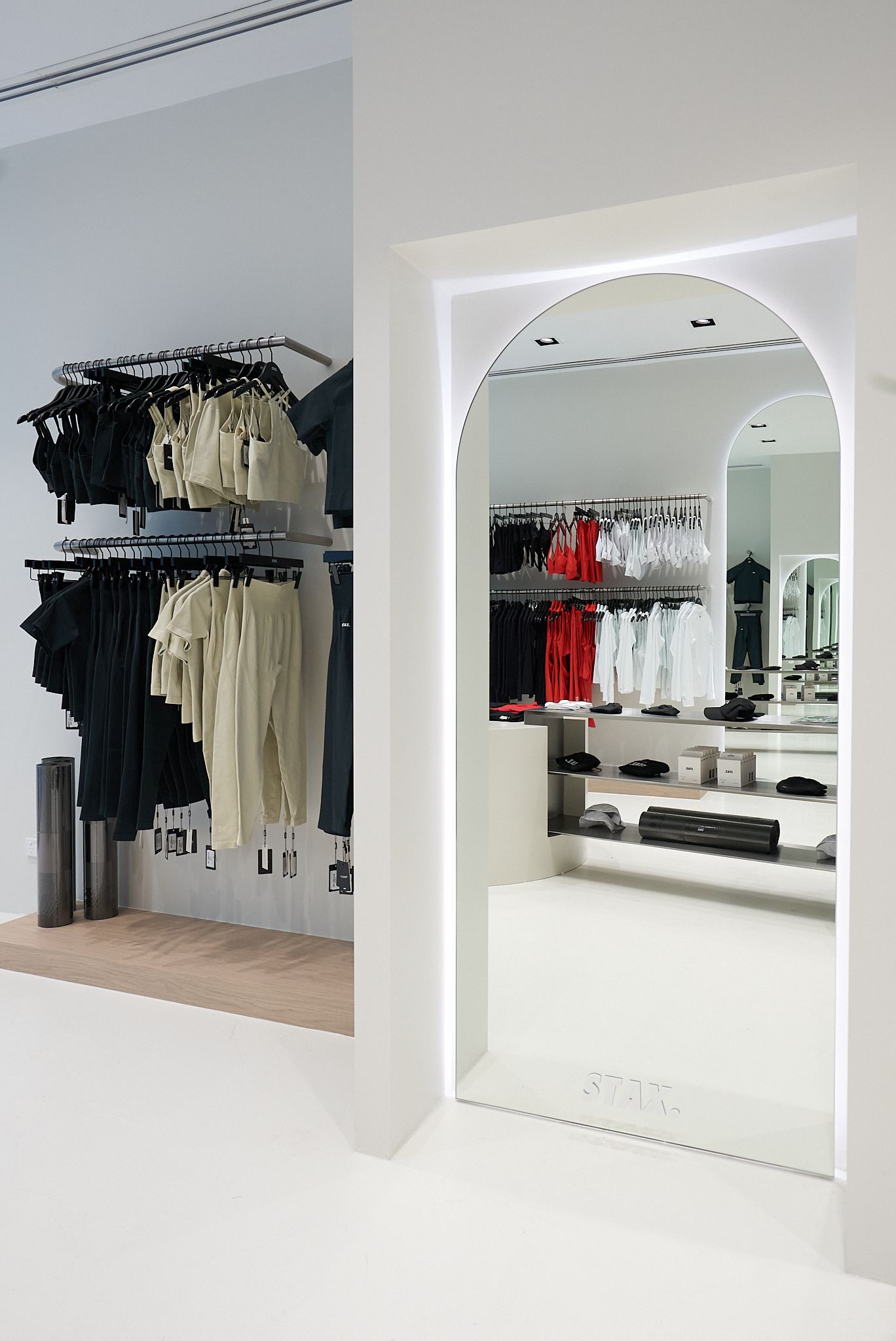 Interior view of a clothing store with white walls and an arched doorway; clothes hang on racks.