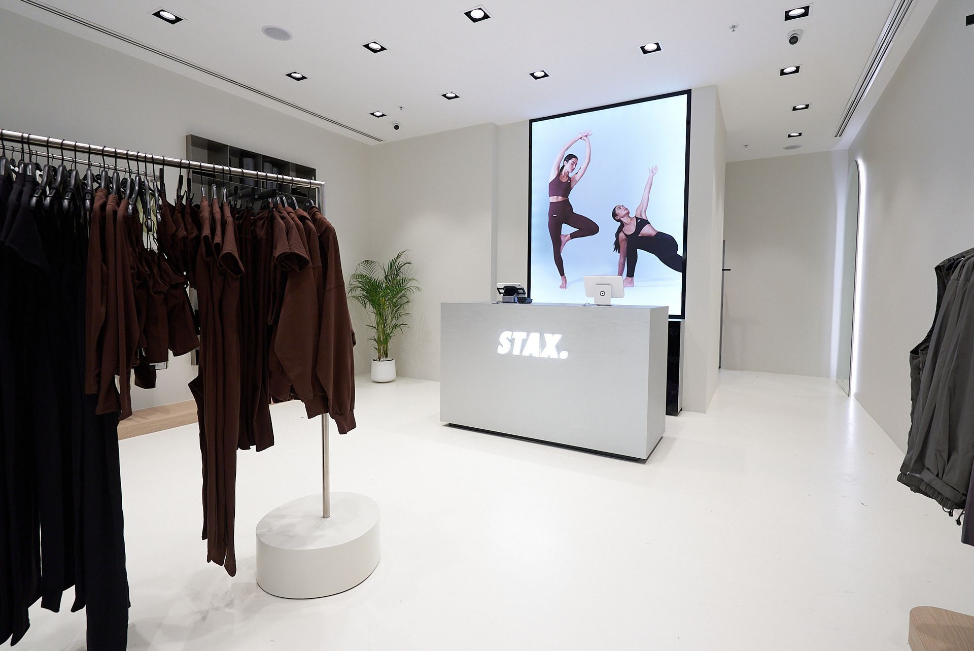 Clothing store interior with clothing racks, a front desk, and a video screen displaying dancers.