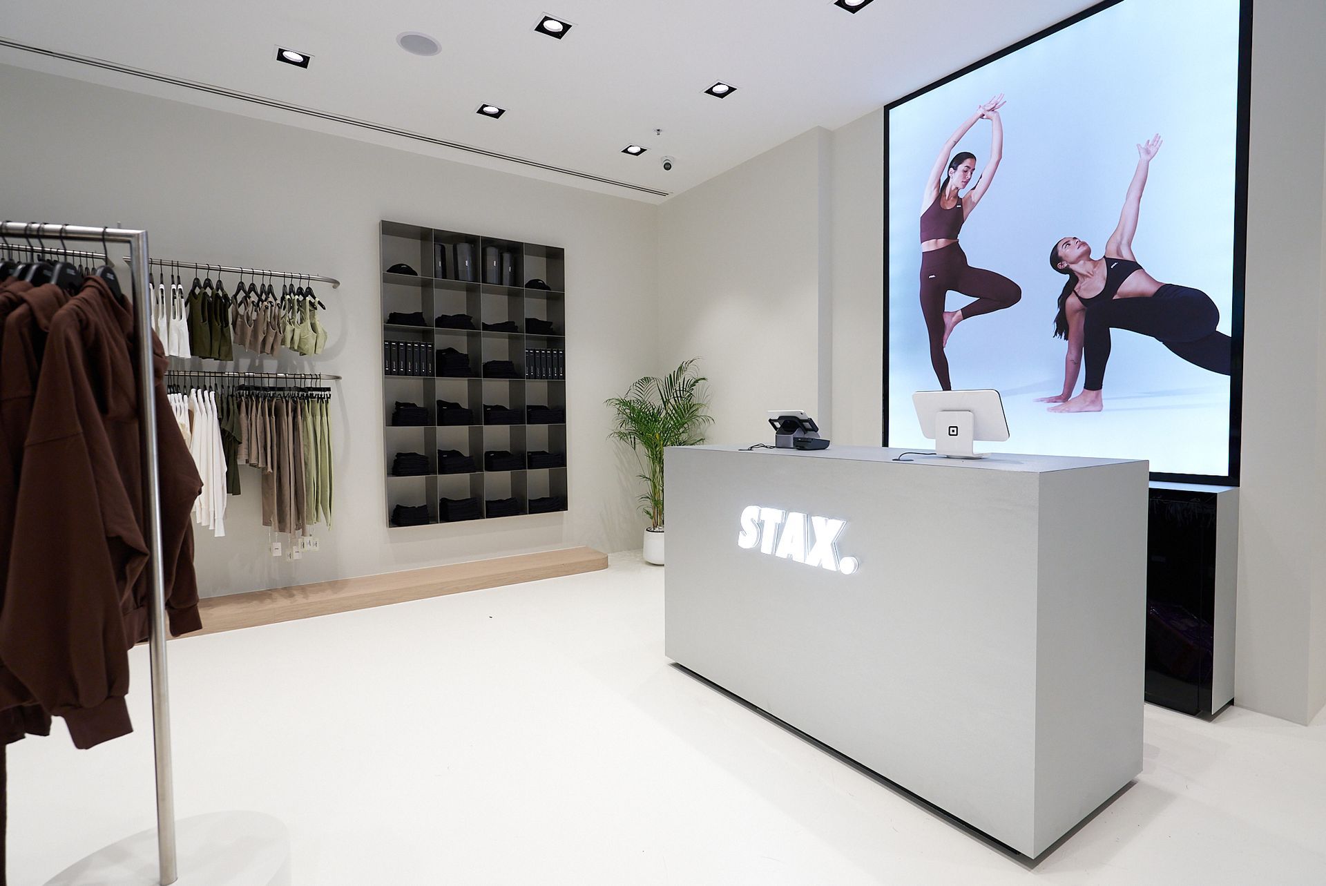 Interior of a STAX. store with merchandise racks, a display screen, and a cash register.