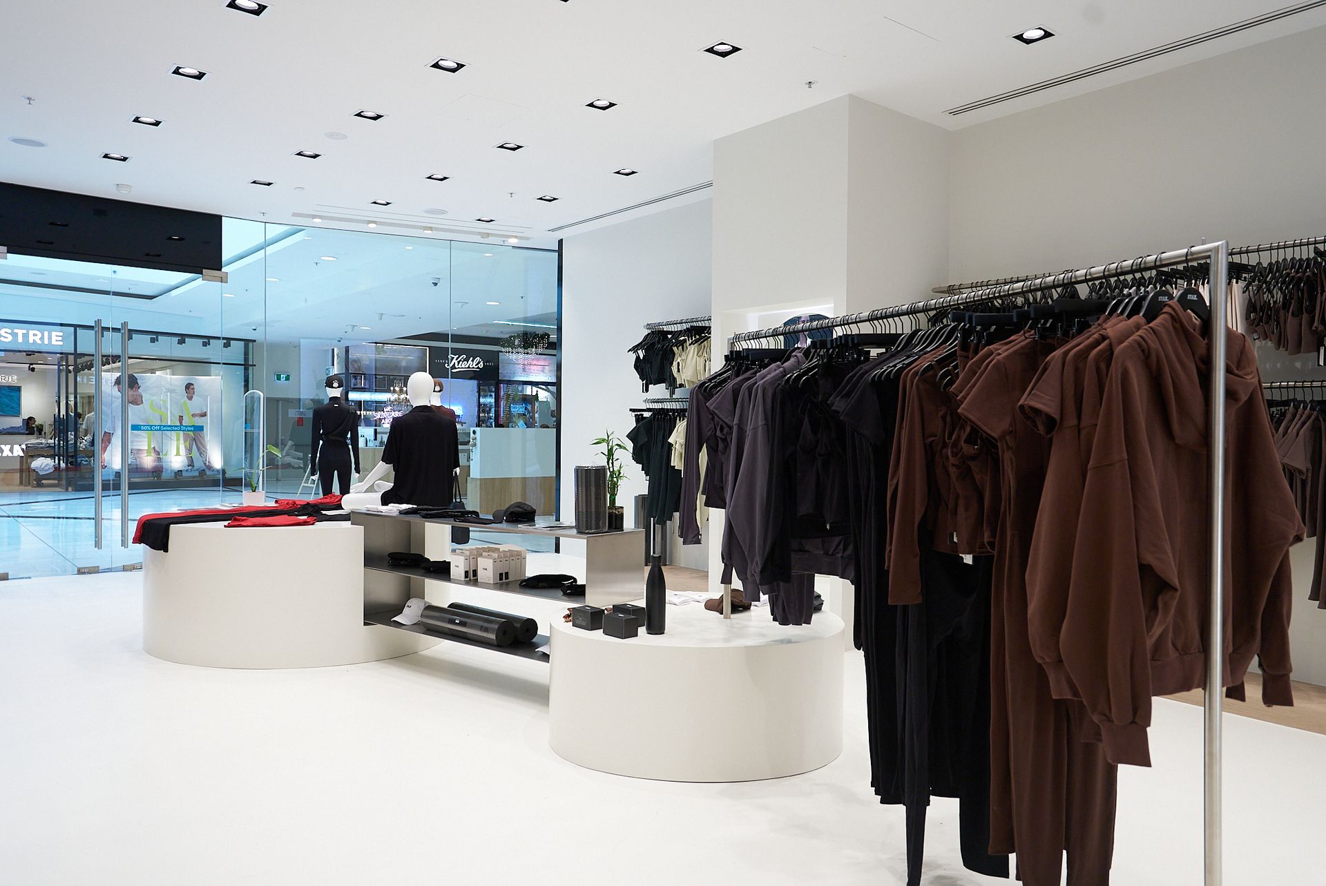 Clothing store interior with racks of clothes and mannequins. White walls, bright lighting.