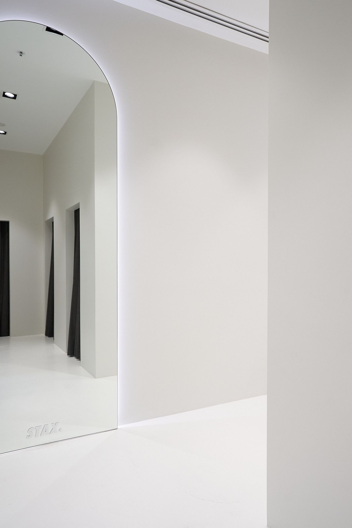 White hallway with arched entrance. Doors line the left wall; bright overhead lighting.