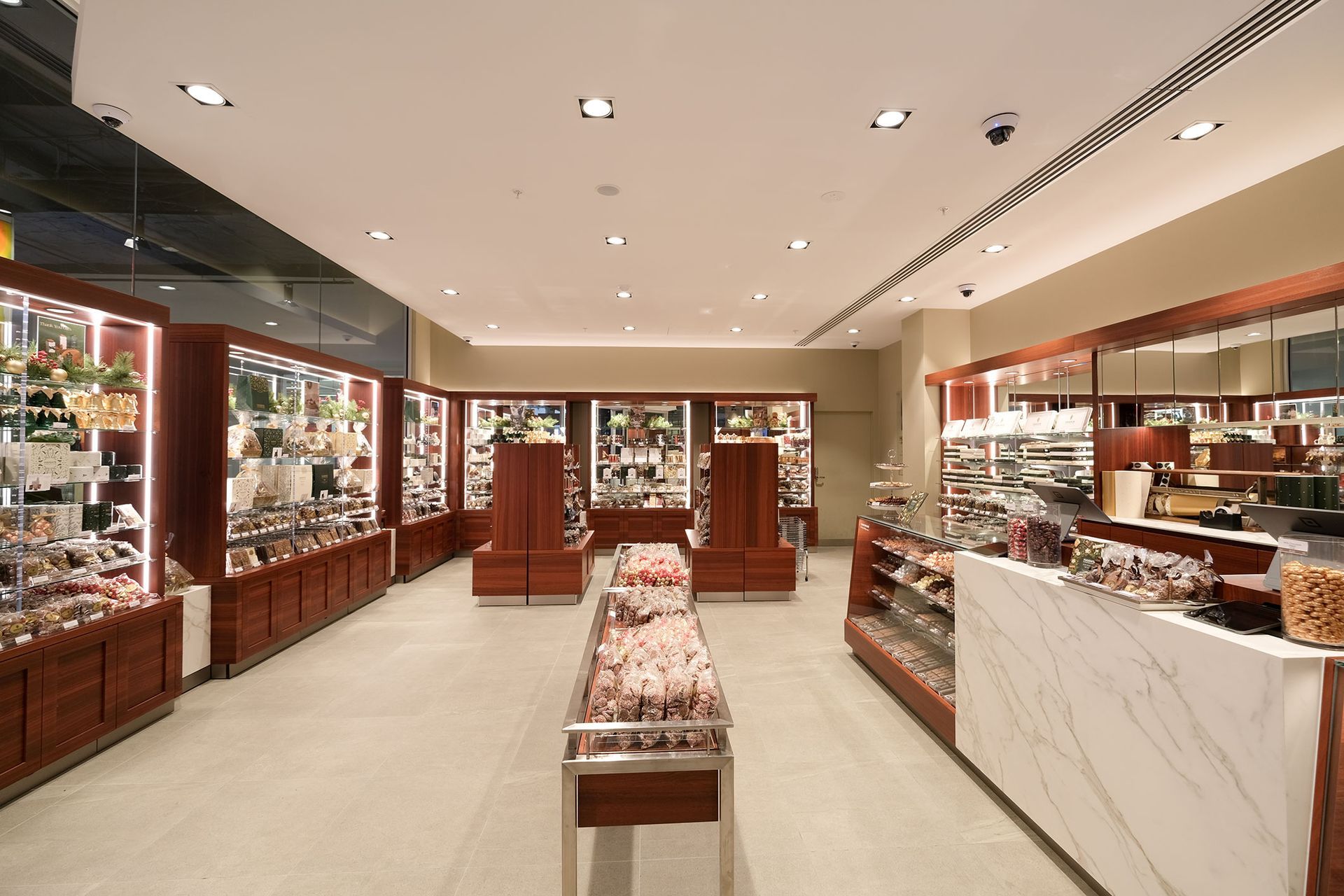Interior of a well-lit candy store with display cases of chocolates and sweets; a white marble counter and light flooring.