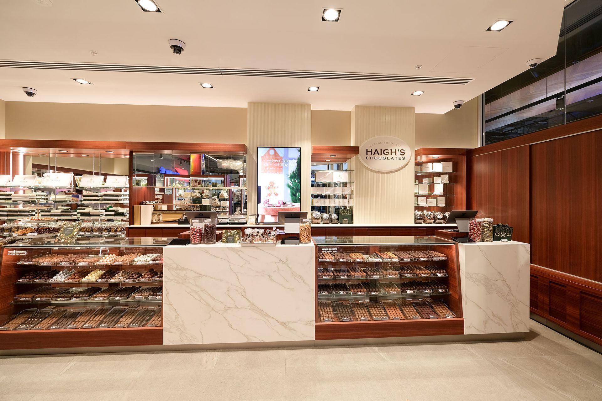 A well-lit confectionery shop with display cases of treats, marble counters, and a digital menu board.