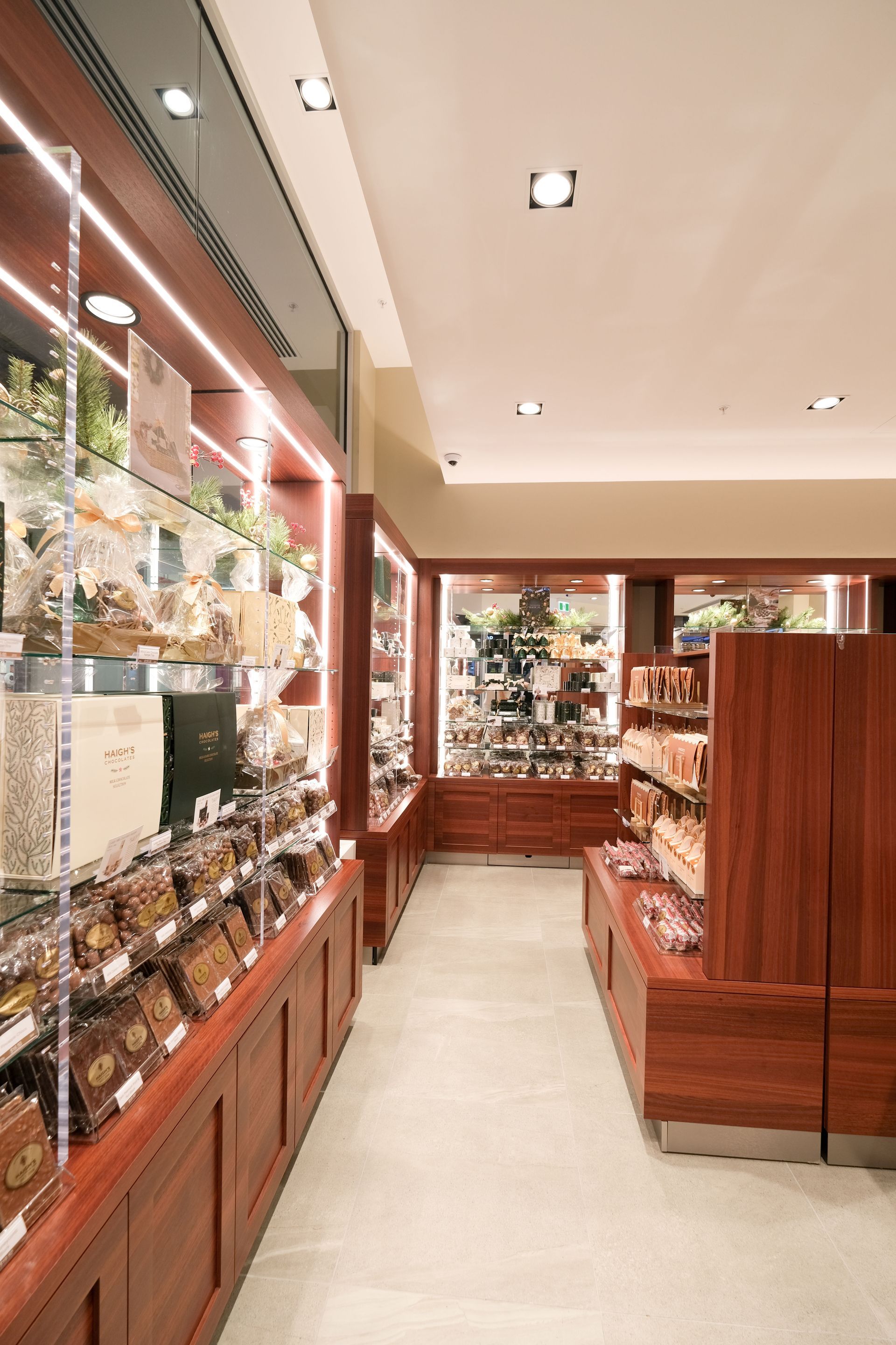 Interior of a shop with wooden display cases filled with packaged goods, warm lighting, and a light-colored floor.