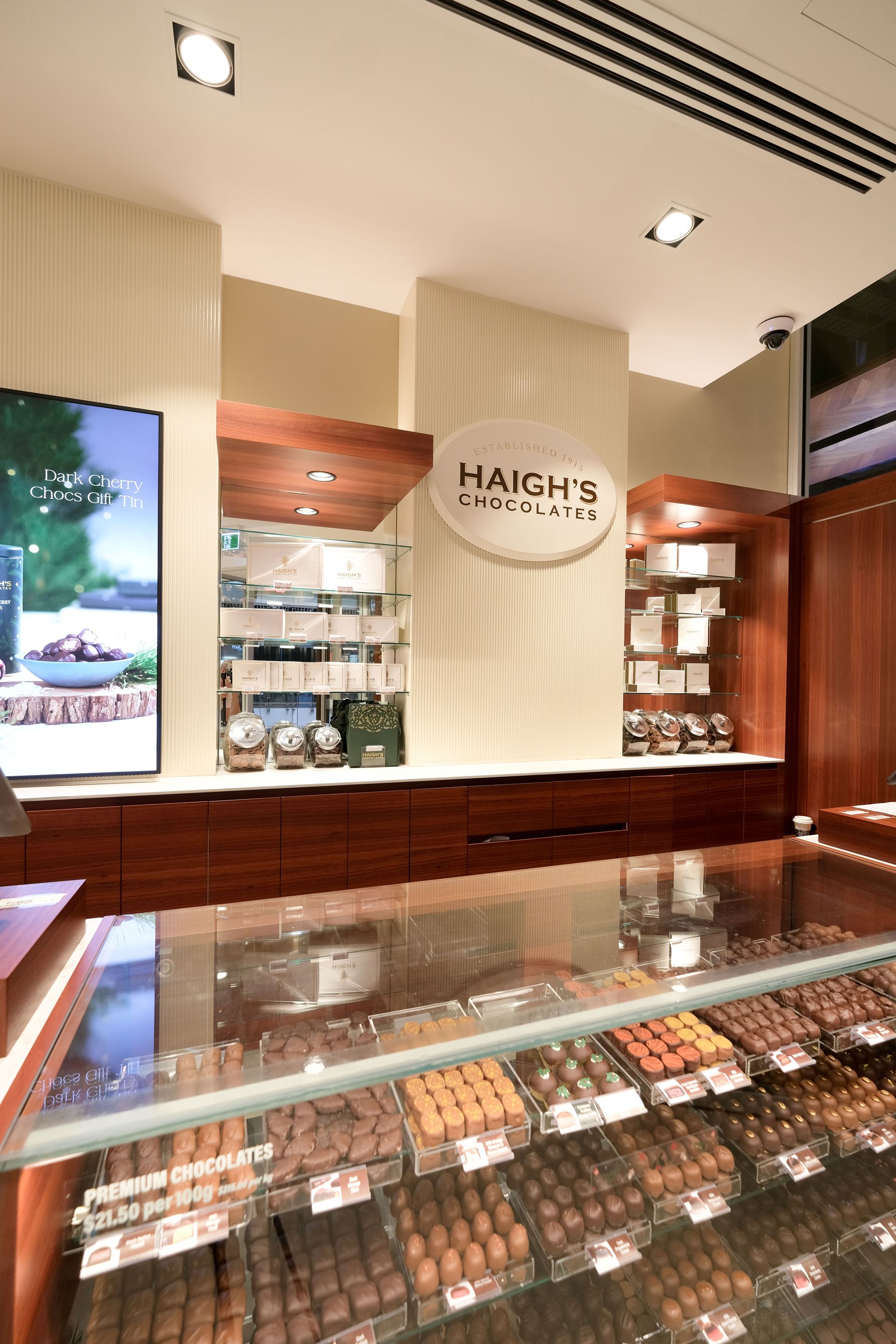 Haigh's Chocolates store interior with glass display case of chocolates, brown wood accents, and sign.