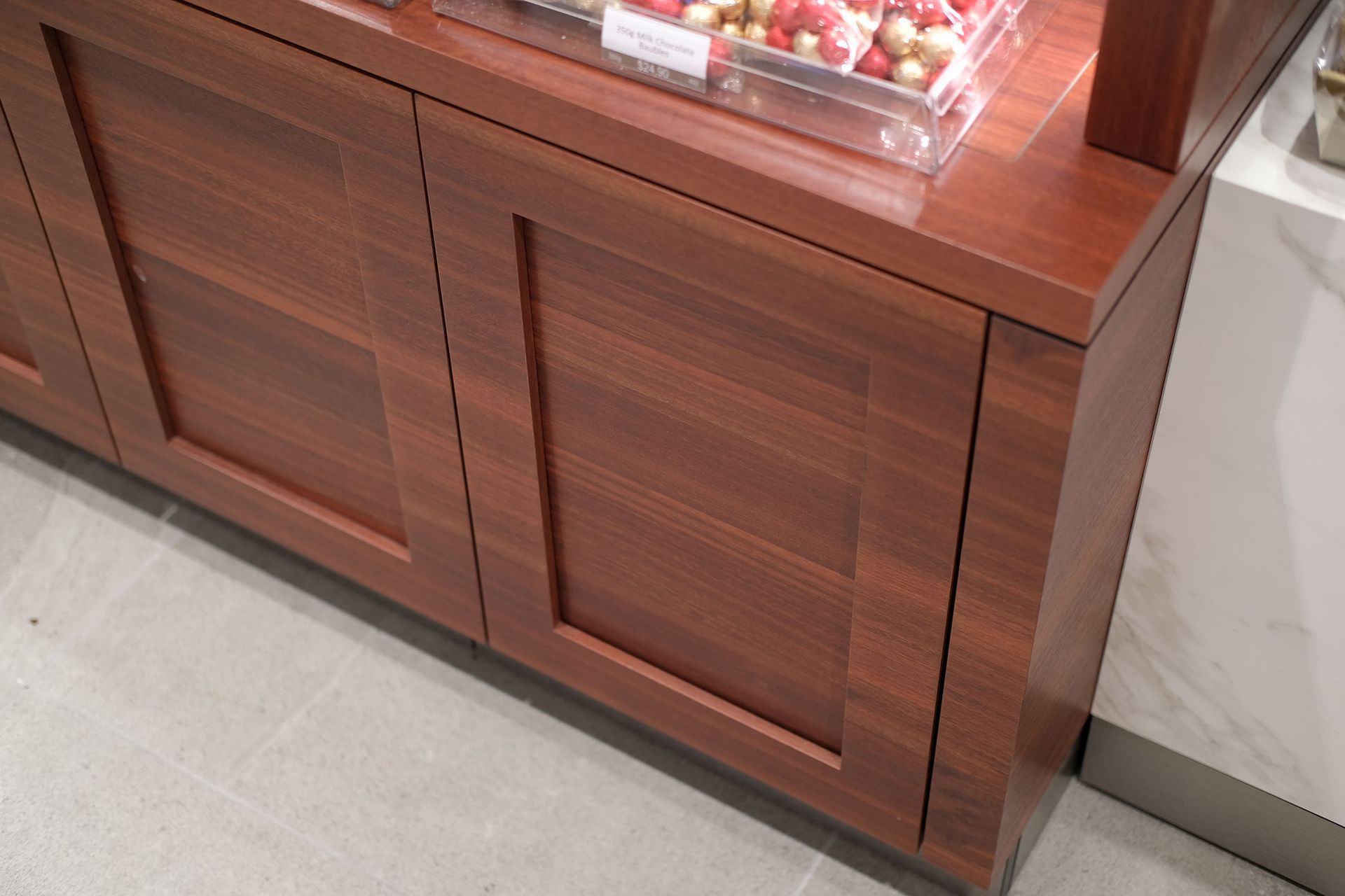 Wooden display cabinet with closed doors, holding food items in clear containers.