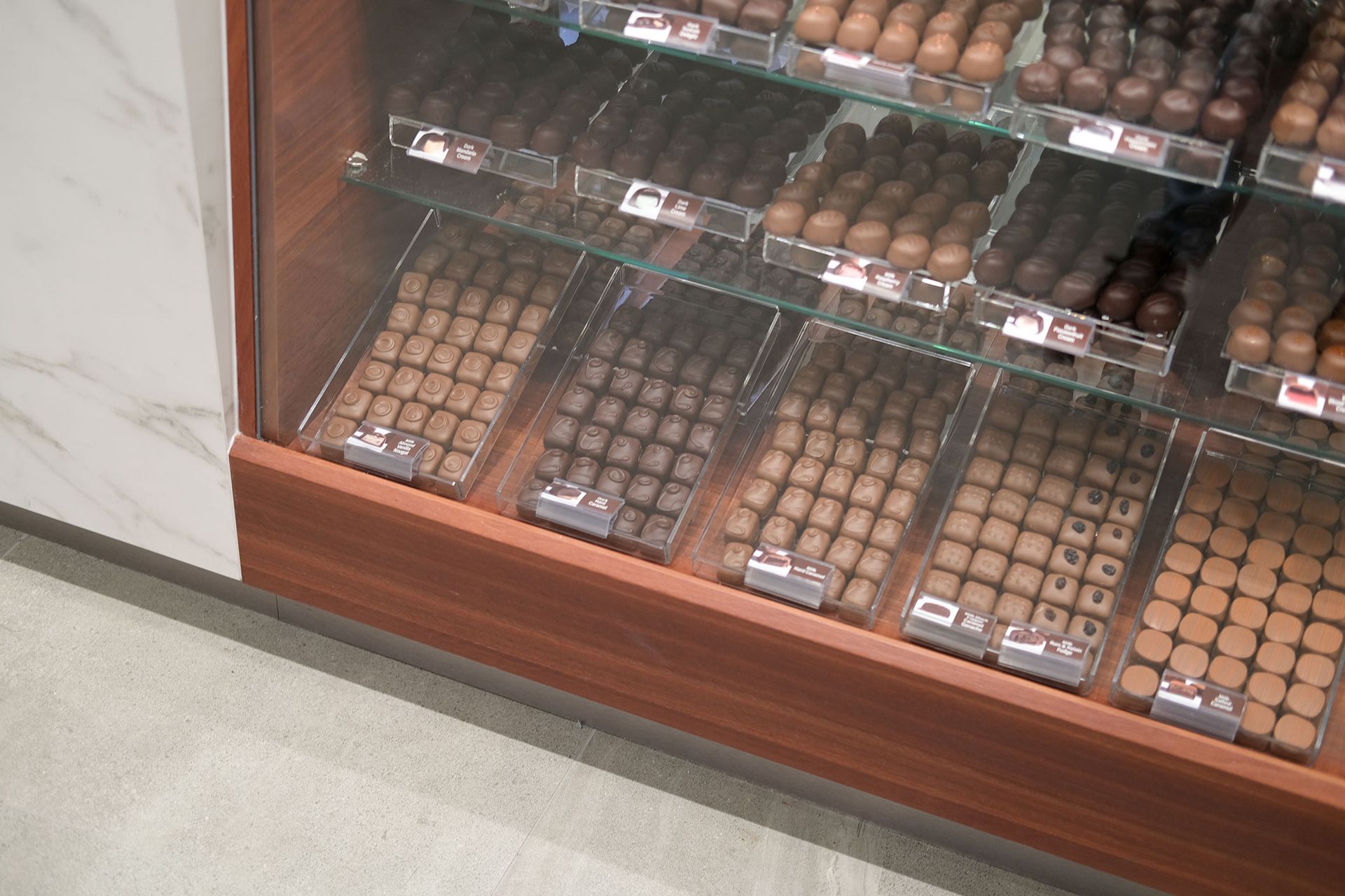 Chocolate candies displayed in a wooden and glass case.