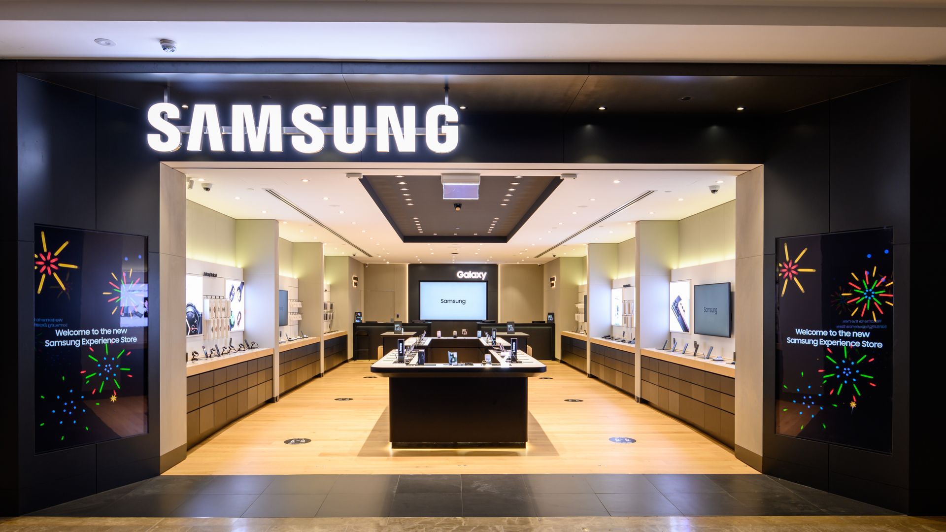 Samsung store entrance with display products. Black and white signage, dark interior.