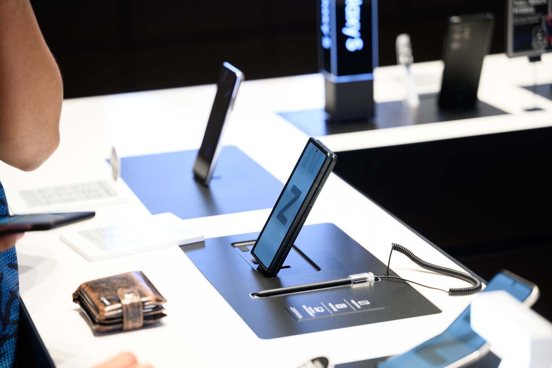 A display table with smartphones and a wallet. A person looks at the devices on display.
