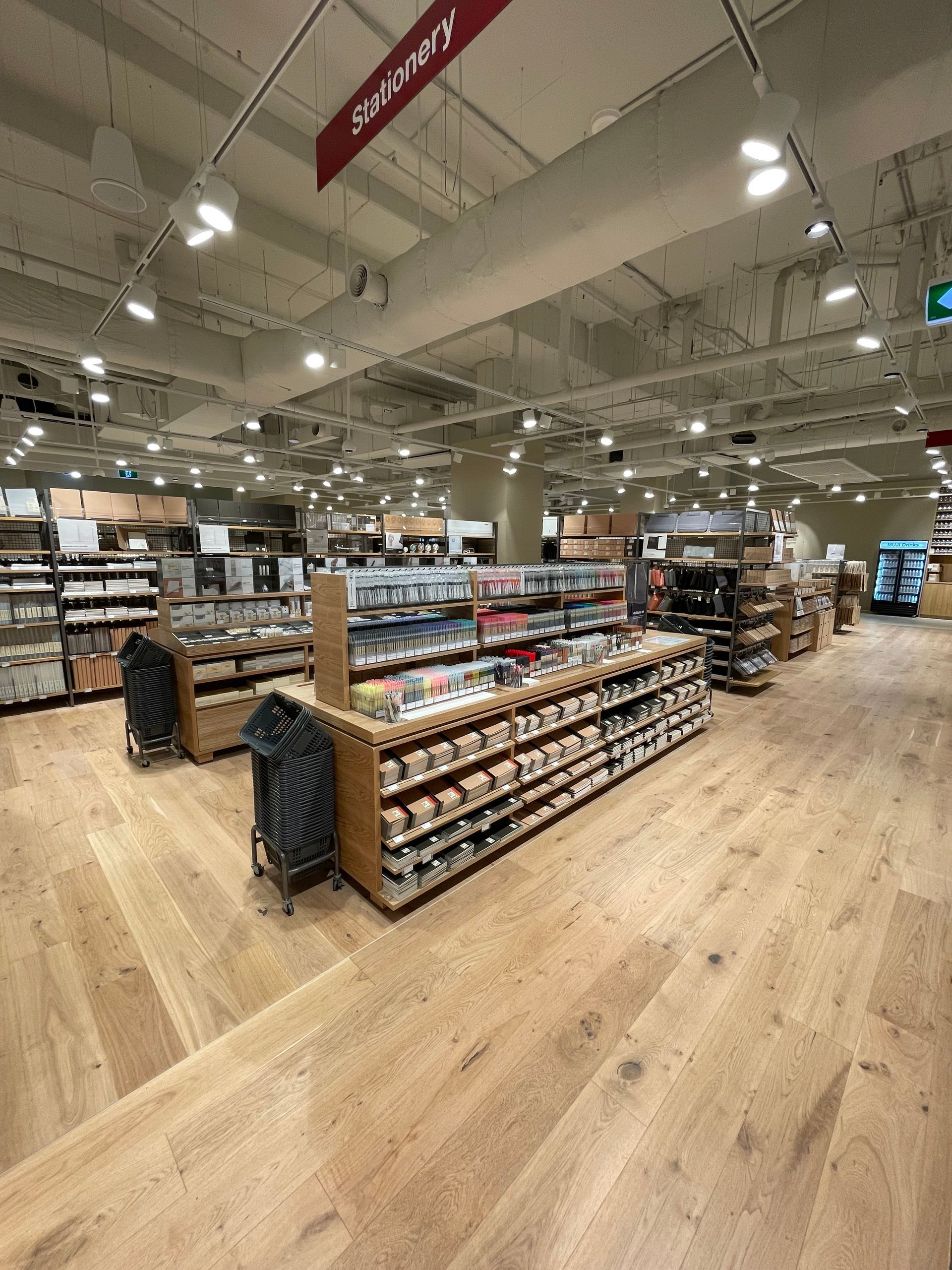 Spacious store interior with wooden floors and shelves stocked with products; overhead lighting.
