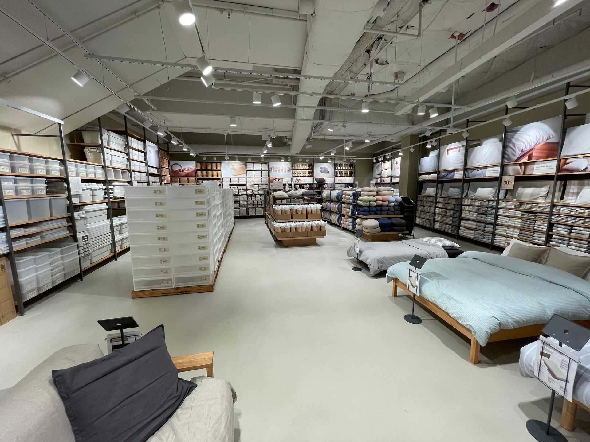 A well-lit store interior with bedding and storage. Wooden display beds and shelves with various items.