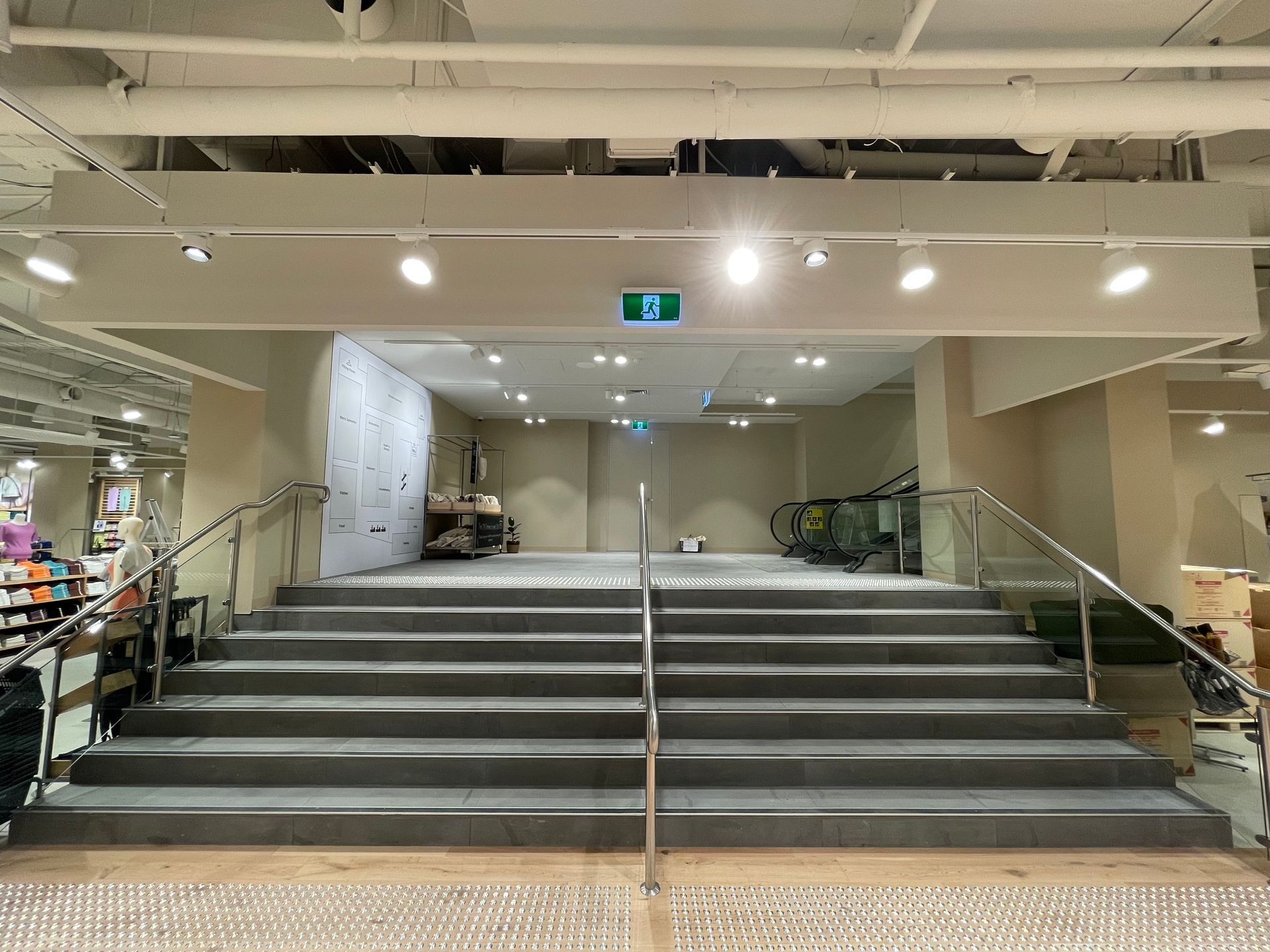 Staircase leading to a landing, with handrails, exit sign, and overhead lights.