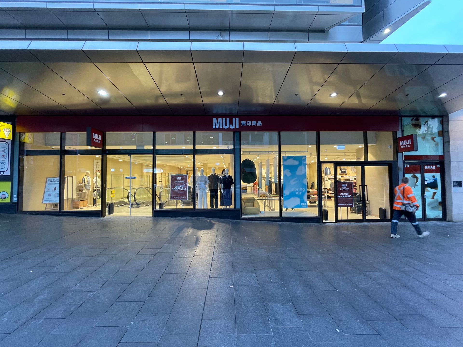 MUJI store exterior with glass windows; a person walks by.